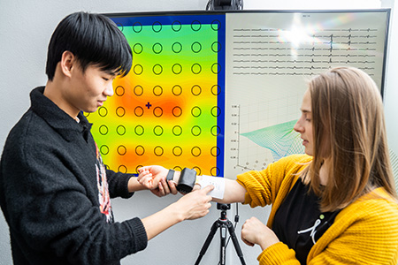 Two people with measuring equipment in front of a screen.