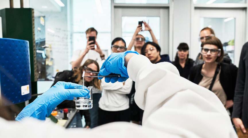 A group of people in a lab looking at a person holding up a beaker. 