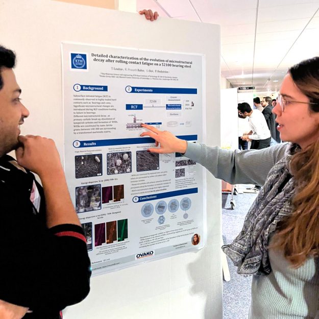 Two students in front of a poster, discussing.