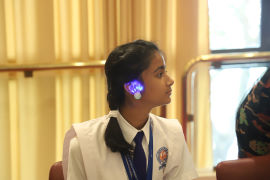 En sittande tjej som bär ett lysande örhänge hon tillverkat under workshopen.