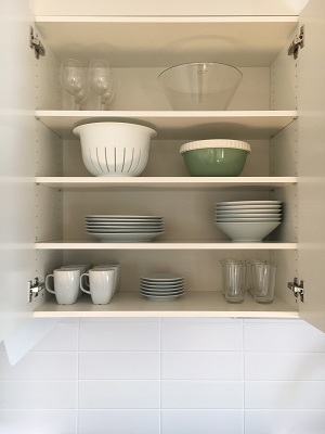 Mugs, dishes, glasses, bowls placed in open cupboards in kitchen.