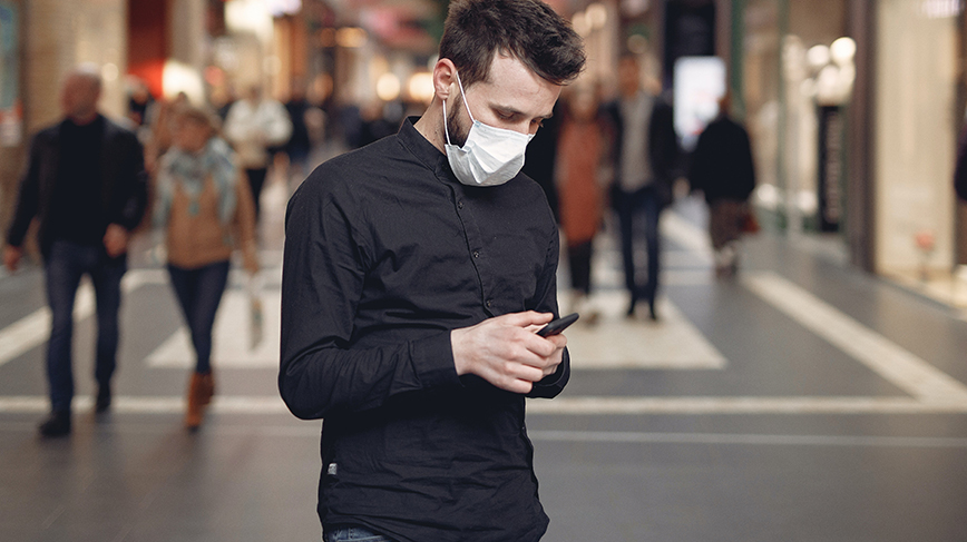 Man wearing a face mask is using his mobile phone in a shopping center.