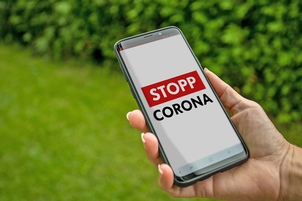 En bild på en hand som håller i en mobiltelefon där appen Stopp Corona visas.