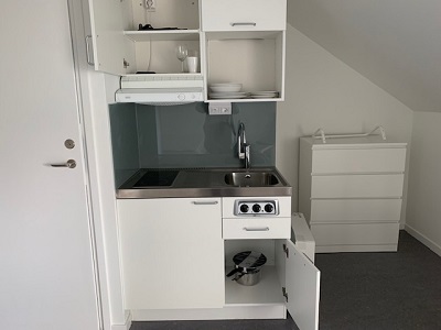 Pentry kitchen with sink, stovetop and fridge, dishes in cupboards.