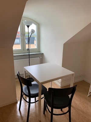 Two black chairs and white table in apartment next to window.