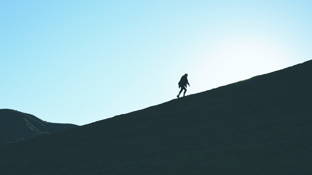 Människa vandrar uppför kulle i motljus.