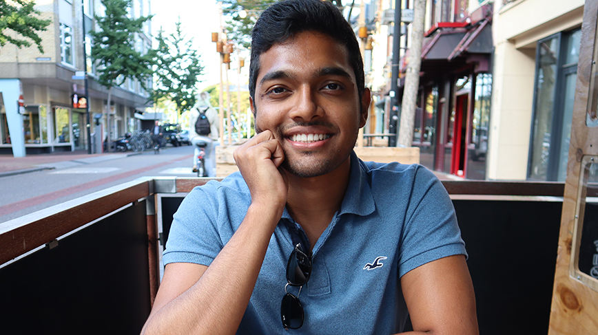 Student poses for camera, seated at a table outside