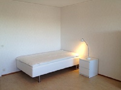 Apartment painted white with bed, nightstand and lamp.