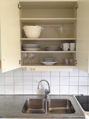 Open kitchen cupboard to show dishes, mugs, bowls and plates.