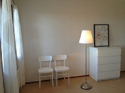 Room of apartment with chairs, dresser, lamp and picture.