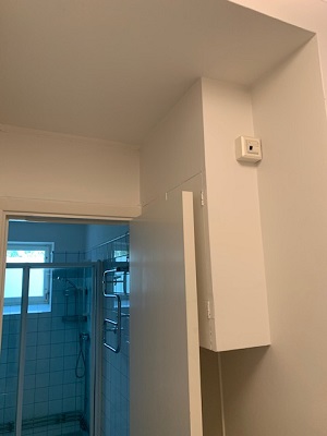 Open door to bathroom, white box attached to wall with small cablebox attached.