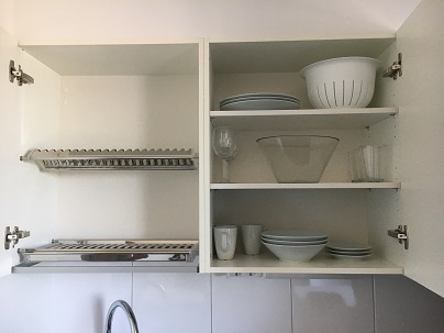 Open cupboard doors to show dishes, glasses, mugs, and bowls.