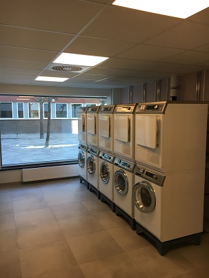 Stacked washers and dryers in large room with windows to the walkway outside.