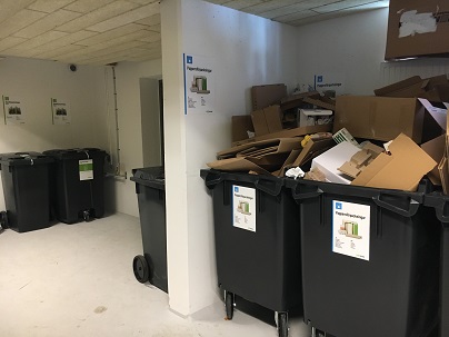 Large green bins in recycling room with cardboard in them.
