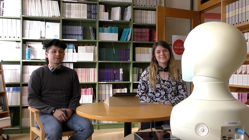 Two people sitting across from a robot. 
