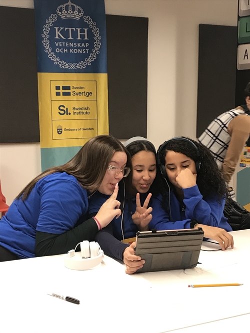  Three girls look at a tablet and make v-signs with their fingers.