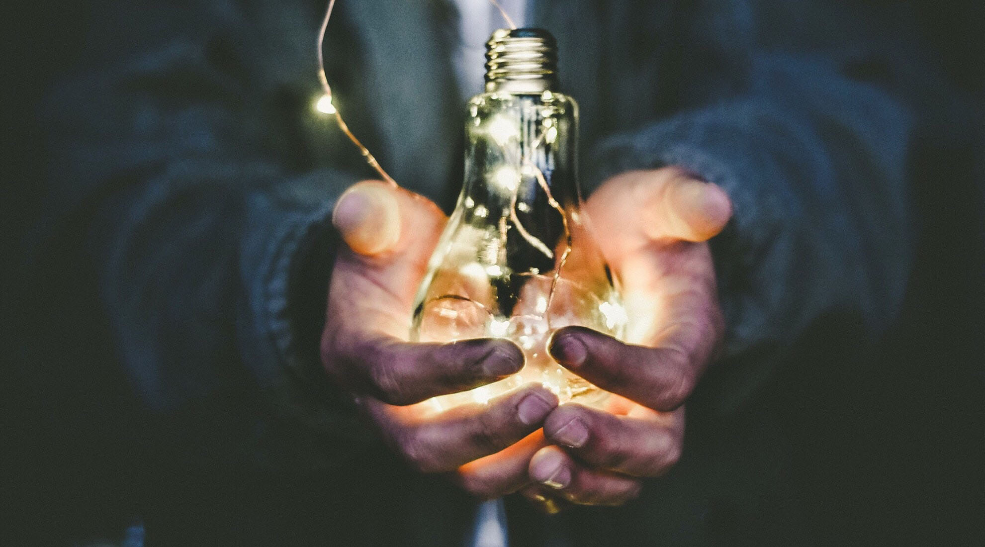 Hands holding a lit lightbulb