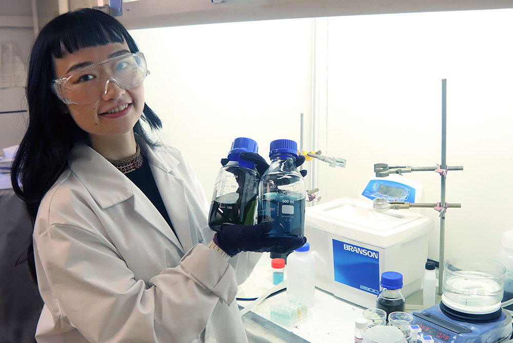 KTH-forskaren Xiong Xiao håller i två behållare framför ett dragskåp i ett labb.
