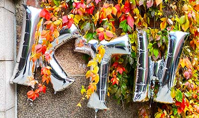 Three silver balloons spelling KTH against an ivy and brick background
