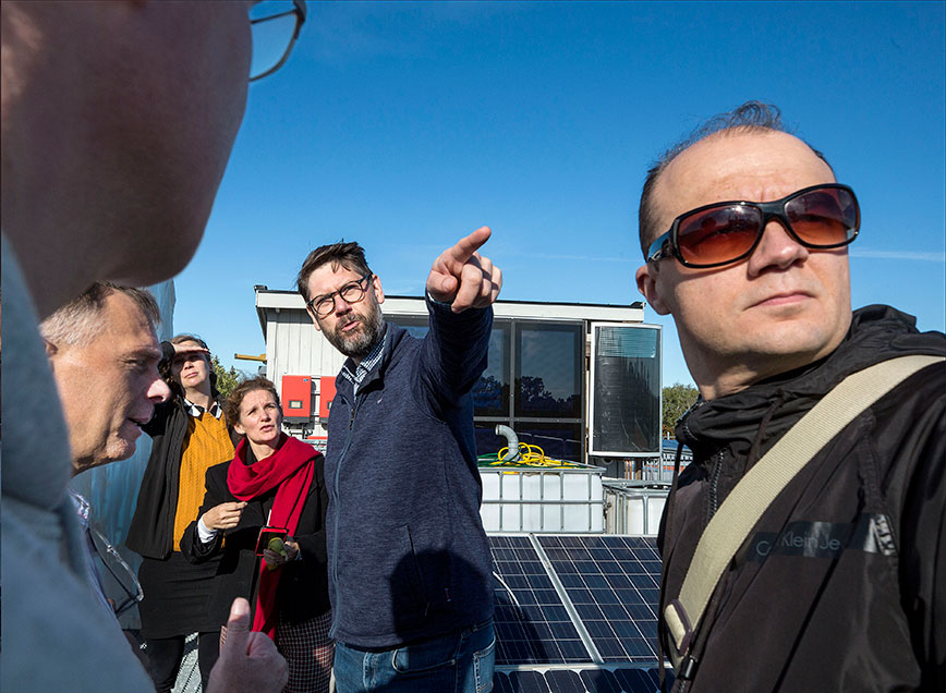 A group of people standing on a roof where there is solar panels.