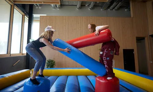 Två studenter som försöker putta ner varandra i en uppblåsbar inhängnad
