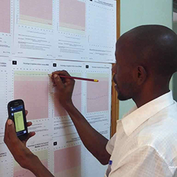 A health worker in Uganda fills out a patient form with a mobile phone and pen