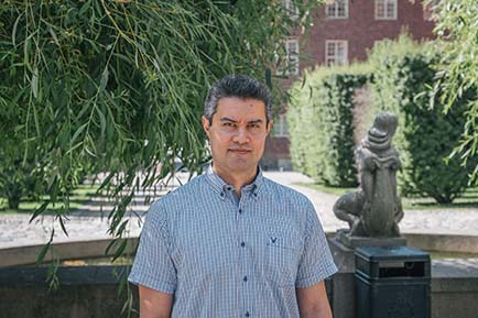 Portrait of Rustam Nabiev on KTH Campus. Trees and brick building in the background.