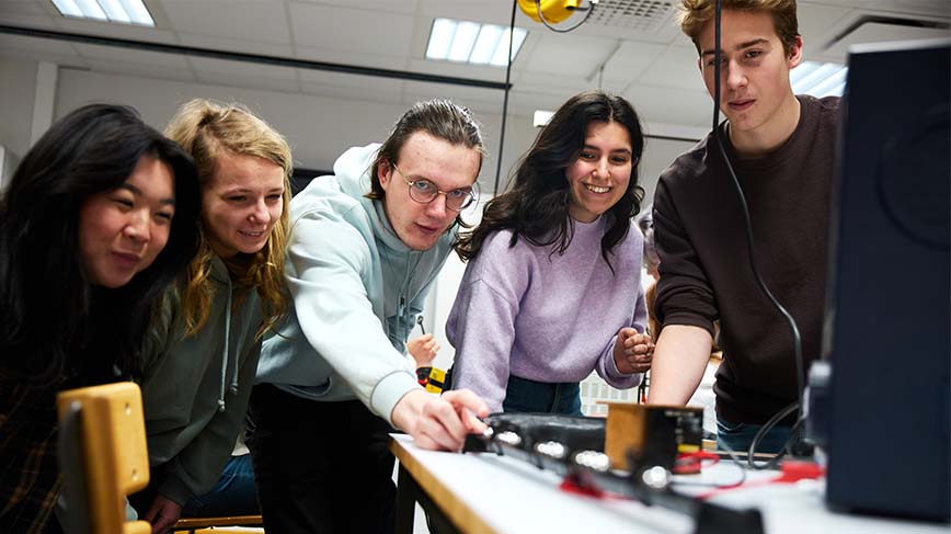 Fyra gymnasieelever och besöksledaren Piltan Gundogan slungar iväg en magnet i ett experiment.