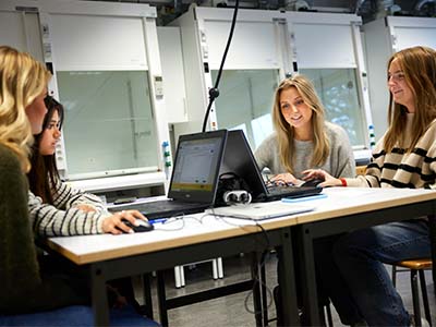 Fyra elever sitter i ett klassrum framför datorer.