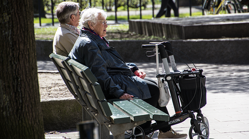 Två äldre personer sitter på en bänk utomhus