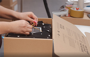 En närbild på en person som packar en låda med plagg. 