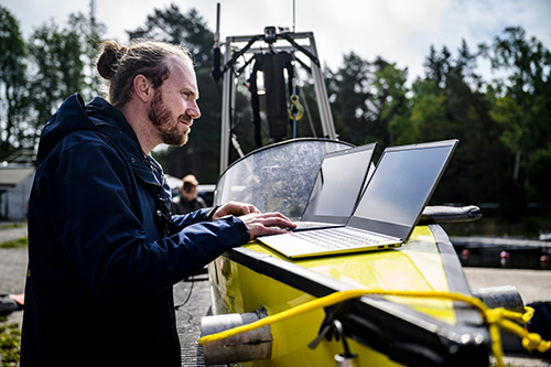 One person is standing in front of two laptops that are placed on a test boat.