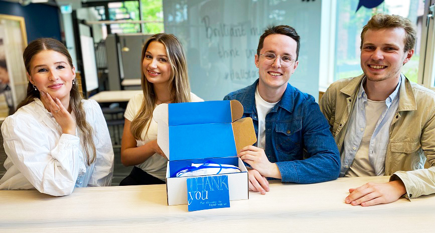 The four founders of Pastisch at a table. In front of them is a box clad in blue paper. 