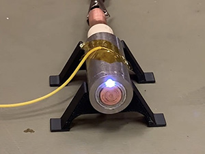 A thruster firing with a small white light. It is about the size of an A battery with a yellow cord.