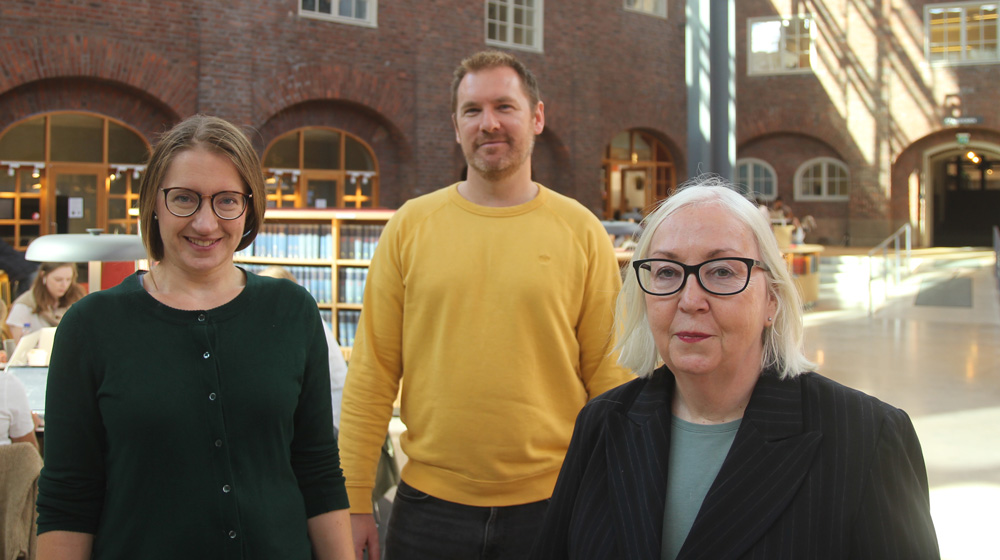 Two women and one man standing in KTH's library smiling into the camera. 