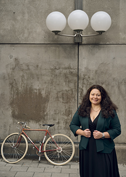 Claudia Olsson in front of a concrete wall, a bicycle and lamp post