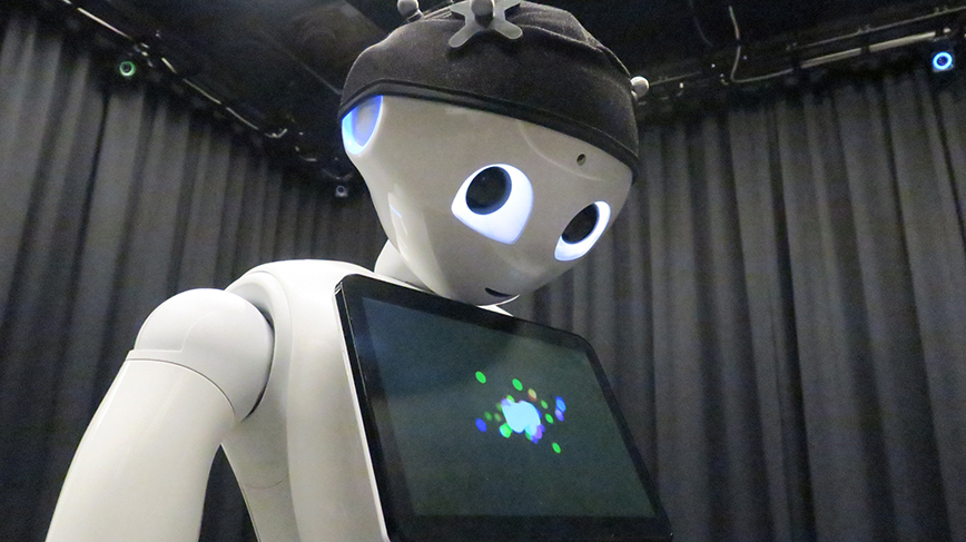 A white plastic robot stars into the camera in a black room