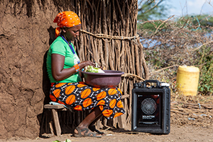 kvinna i afrikansk by som tvättar grönsaker i ett kärl med vatten från en Solvattenrenare intill