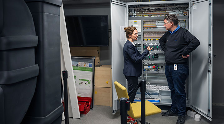 A man and a woman standing in front of an electrical cabinet.
