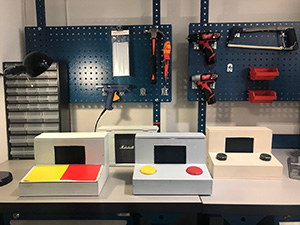 Funki's instruments, white boxes with large yellow and red buttons, with tools on the wall behind.