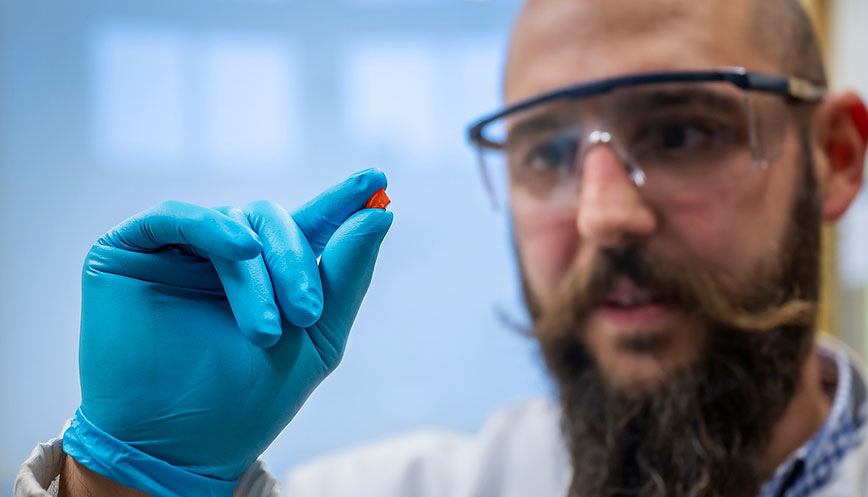 A researcher with safety glasses holding a tiny solar cell material. 
