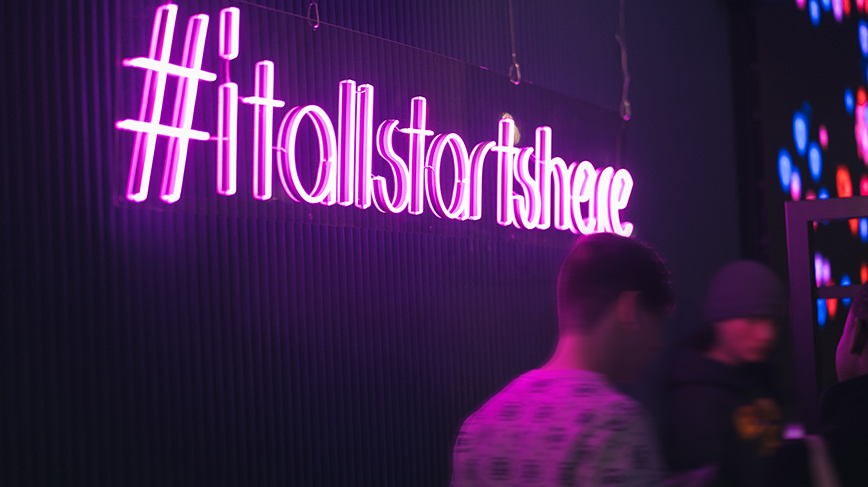  Dark room with neon sign that reads: "It all starts here"