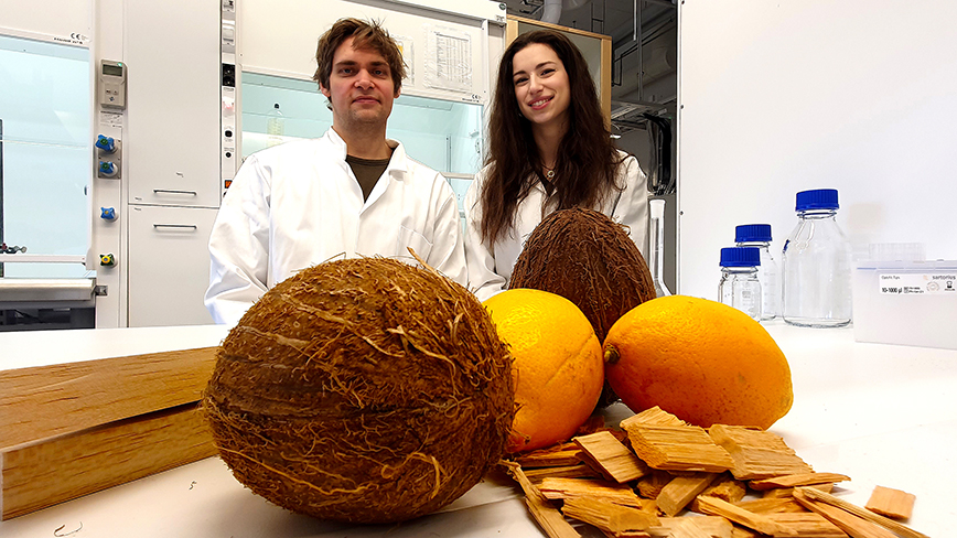 Coconuts and lemons in the foreground on a countertop in the lab. Behind them, two scientists. 