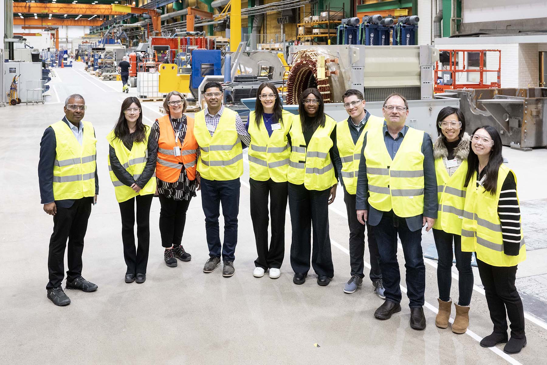 Gruppbild på studenter i grula västar i en industribyggnad. 