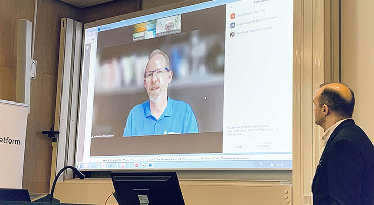 A man in a blue shirt presenting via a link on a screen.