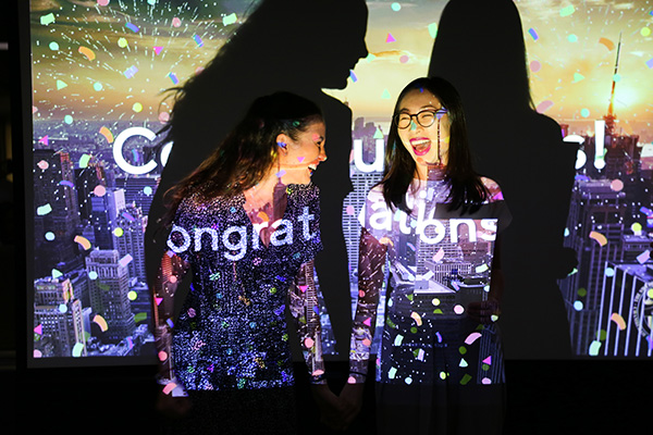 Two women do a high five in front of a screen showing confetti