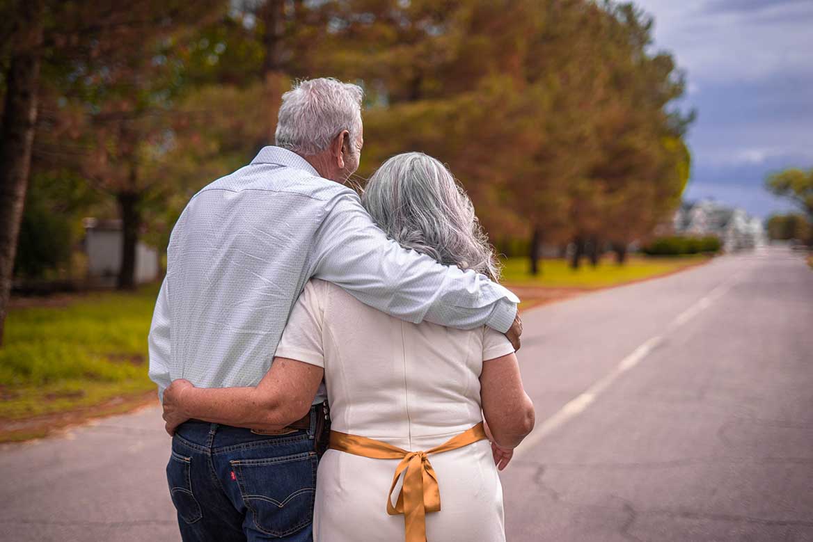 Ett äldre par promenerar på en väg och håller om varandra.