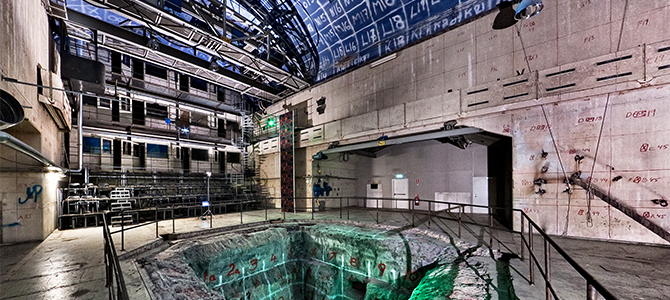 Bild inifrån KTH:s reaktorhall. En stor lokal med betongväggar och stor ihålighet i mitten.
