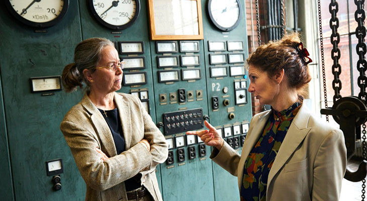 Two women talking in front of an old control panel.