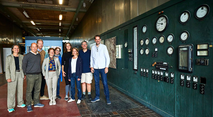 A group of people standing beside a wall of old control panels.